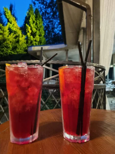 Gece kulübündeki ahşap bir masada buzlu bardakta kırmızı kokteyl.