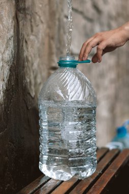 İnsan doğal bir kaynaktan plastik şişeye temiz kaynak suyu döker. Bütçe açığı, kriz, içme suyu kıtlığı Ukrayna 'da bir sorundur. Kavramsal fotoğraf. Su tüketimi ve rezervasyon kavramı 