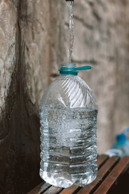 Doğal bir kaynaktan plastik şişeye taze kaynak suyu dökülüyor. Bütçe açığı, kriz, içme suyu kıtlığı Ukrayna 'da bir sorundur. Kavramsal fotoğraf. Su tüketimi ve rezervasyon kavramı 