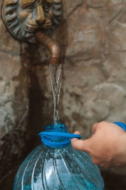İnsan doğal bir kaynaktan plastik şişeye temiz kaynak suyu döker. Bütçe açığı, kriz, içme suyu kıtlığı Ukrayna 'da bir sorundur. Kavramsal fotoğraf. Su tüketimi ve rezervasyon kavramı 