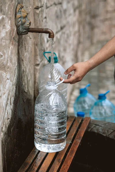 Man pour fresh spring water into plastic bottle from a natural source. Deficit, crisis, shortage of drinking water is a problem in Ukraine. Conceptual photo. Water consumption and reservation concept