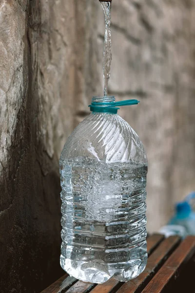 Pouring fresh spring water into plastic bottle from a natural source. Deficit, crisis, shortage of drinking water is a problem in Ukraine. Conceptual photo. Water consumption and reservation concept