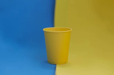 Sarı-mavi arka planda tek kullanımlık sarı kağıt bardak, izole nesne, fotokopi alanı olan fotoğraf. Logo için maket, yan görüş. Ukrayna ulusal renkleri