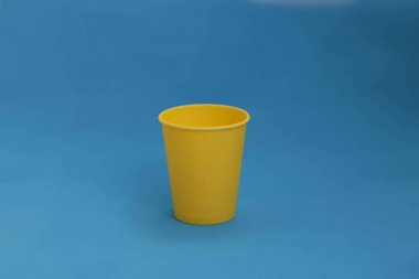 Mavi arka planda tek kullanımlık sarı kağıt bardak, izole nesne, fotokopi alanı olan fotoğraf. Logo için maket, yan görüş. Ukrayna ulusal renkleri
