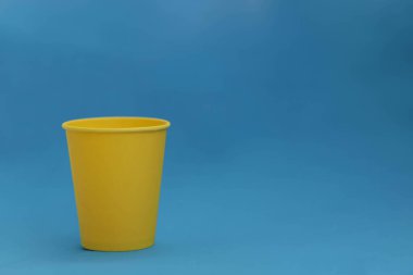 Mavi arka planda tek kullanımlık sarı kağıt bardak, izole nesne, fotokopi alanı olan fotoğraf. Logo için maket, yan görüş. Ukrayna ulusal renkleri