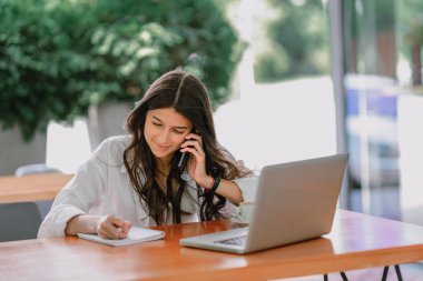 Portre mutlu genç ofis asistanı uzaktan bilgisayarla, tabletle ve kahveyle çalışıyor terasta dizüstü bilgisayarda notlar alıyor ve akıllı telefonu kontrol ediyor. Uzak bağımsız başarılı iş