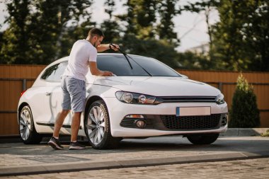 Man is wiping the car with a microfiber cloth. Contactless self-service car wash. Personal car care cleaning outside. Concept disinfection and antiseptic cleaning of vehicle, covid-19 and coronavirus