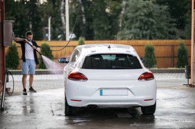 Man washing white car at contactless self-service car wash. Washing sedan car with foam and high-pressure water. Personal car care, cleaning outside. Nozzle spraying a jet of water, process of washing