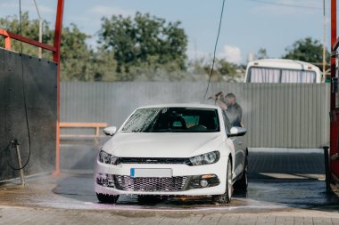  Man washing white car at contactless self-service car wash. Washing sedan car with foam and high-pressure water. Personal car care, cleaning outside. Nozzle spraying a jet of water, process of washing