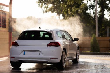 White car sedan at contactless self-service car wash at sunset. Personal car care cleaning outside in summer. Concept disinfection and antiseptic cleaning of vehicle, covid-19 and coronavirus