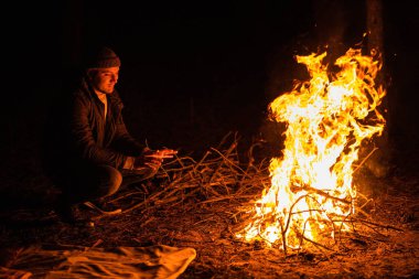 Alevlerin yanında oturan adam, gecenin bir yarısı nehir kıyısında ormanda kıvılcımlar saçan şenlik ateşi kalıntıları. Kömürleşmiş ağaç dalları. Yakacak odun yakıyor. Büyük parlak bir alev. Yakın plan, seçici odak