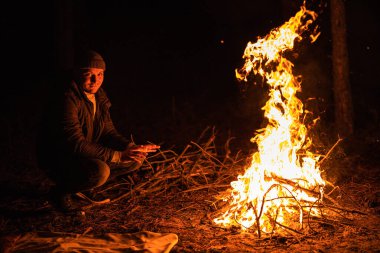 Alevlerin yanında oturan adam, gecenin bir yarısı nehir kıyısında ormanda kıvılcımlar saçan şenlik ateşi kalıntıları. Kömürleşmiş ağaç dalları. Yakacak odun yakıyor. Büyük parlak bir alev. Yakın plan, seçici odak