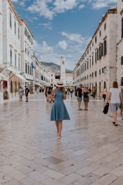 Dubrovnik, Hırvatistan - 21 Eylül 2021: Güzel bayan turist, mavi elbiseli ve hasır şapkalı gezgin ana cadde boyunca yürüyor. Eski kasaba 1979 yılında Avrupa 'da UNESCO Dünya Mirasları Listesi olarak listelendi.