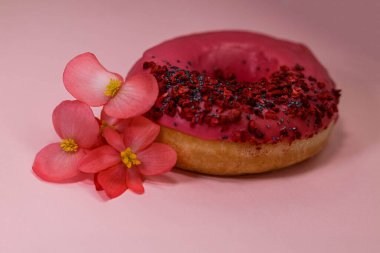 Pembe buzlu çörek ve renkli serpinti, haşhaş tohumu ve pembe arka planda yenilebilir begonya çiçekli ahududu. Lezzetli, yağlı, yüksek kalorili tatlı yiyecekler. Seçici Odaklanma