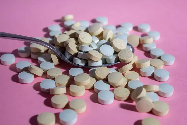 Multicolored round medical pills scattered from a spoon on a pink background, vertical image — Stok fotoğraf