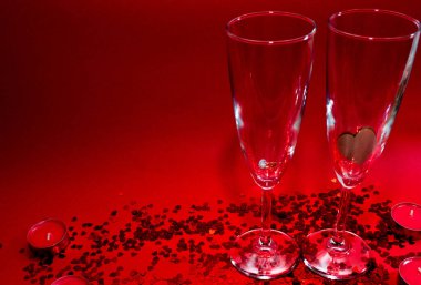 Şampanya kadehleri, kırmızı mumlar, kırmızı arka planda kalp şeklinde kırmızı konfeti.