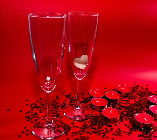 Şampanya kadehleri, kırmızı mumlar, kırmızı arka planda kalp şeklinde kırmızı konfeti. — Stok fotoğraf