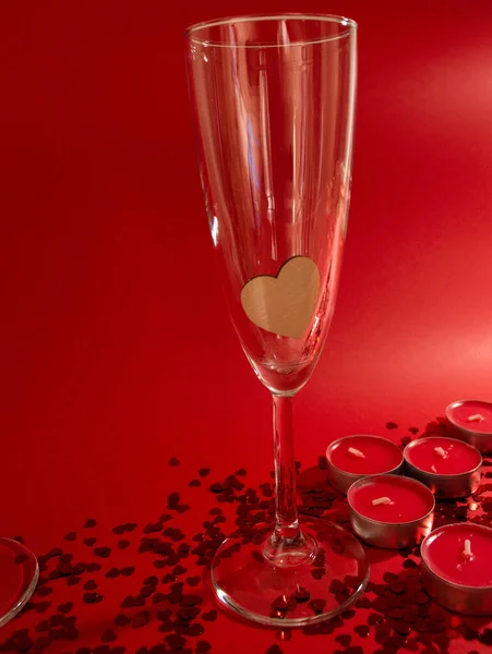 Şampanya kadehleri, kırmızı mumlar, kırmızı arka planda kalp şeklinde kırmızı konfeti. — Stok fotoğraf