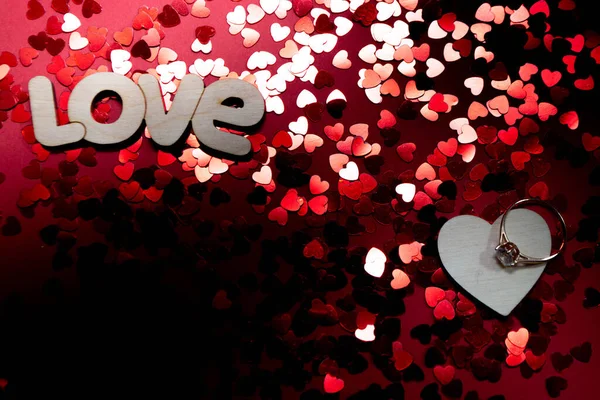 Aşk, kalp ve evlilik yüzüğü. Kırmızı arka planda konfeti. — Stok fotoğraf