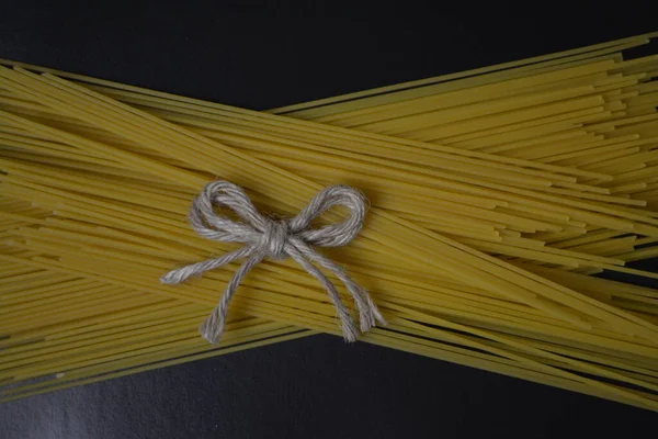 Esparguete cru envolto com corda em um fundo preto, close-up — Fotografia de Stock
