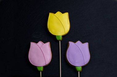 Sarı şeklinde zencefilli çörek. Siyah arka planda pembe ve eflatun laleler. Şenlikli yemek arka planında. Güzel tatlılar kavramı.