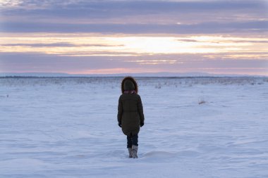 Karlı bir tarlada yalnız bir gencin silueti. Kar tarlası manzarası ve gün batımında dağlar. Doğa ve çocuk kavramı.