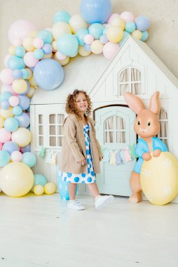 Tavşan kulaklı kız Paskalya avı için renkli yumurta boyuyor. Bahar tatili kutlaması için çiçek, sepet ve tavşanlı ev dekorasyonu..