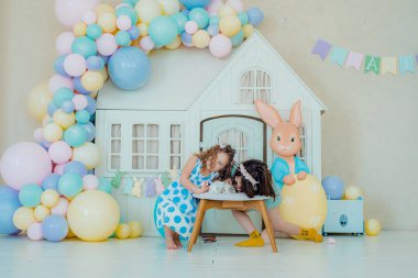 Çocuklar paskalya yumurtalarını boyuyor. Tavşan kulaklı kız Paskalya avı için renkli yumurta boyuyor. Bahar tatili kutlaması için çiçek, sepet ve tavşanlı ev dekorasyonu..