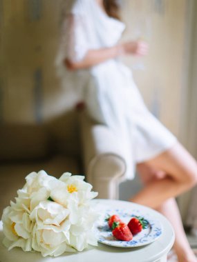on the morning of the bride, lies three strawberries, and a bouquet of daffodils. Against the background is a girl in a nightie