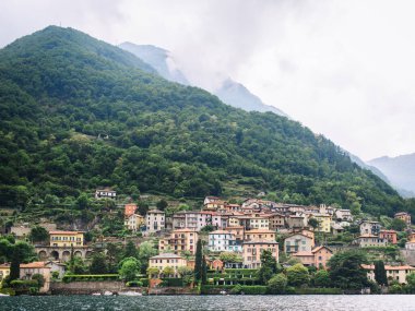 Italy. Lake Como. Green high mountains in the clouds with small houses and villages in red, yellow, and white colors. down below is Lake Como. Overcast