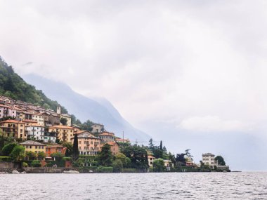 Italy. Lake Como. Green high mountains in the clouds with small houses and villages in red, yellow, and white colors. down below is Lake Como. Overcast