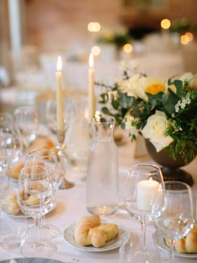 Served beautiful table, three glasses, plates with eucalyptus, breakfast bread, candles and a bouquet