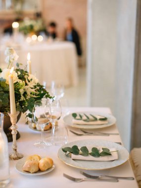 Served beautiful table, three glasses, plates with eucalyptus, breakfast bread, candles and a bouquet
