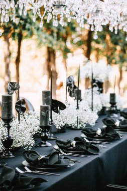 Serving and decorating a banquet table in black with white flowers and black candles at an outdoor party.
