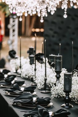 Serving and decorating a banquet table in black with white flowers and black candles at an outdoor party.