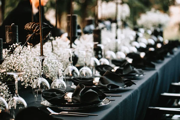 Serving and decorating a banquet table in black with white flowers and black candles at an outdoor party.