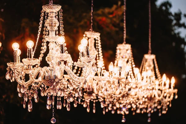 Crystal chandeliers glow in the evening in the park as a decoration.