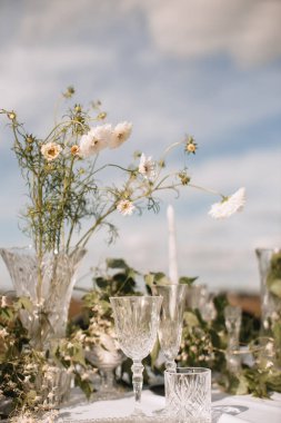 Decor for a wedding ceremony in a picturesque meadow. Wildflowers, crystal glasses, crystal plates, beautiful wedding tableware