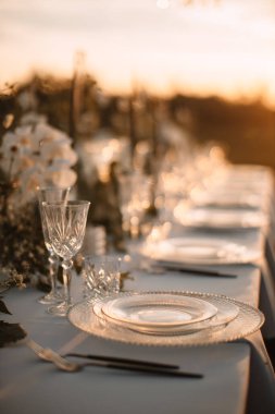 The delicate decor of the wedding banquet table is in pastel colors. Wildflowers, crystal glassware, candles. crystal chandelier on top, illuminating the table. Rays of the setting sun.