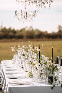 The delicate decor of the wedding banquet table is in pastel colors. Wildflowers, crystal glassware, candles. crystal chandelier on top, illuminating the table.