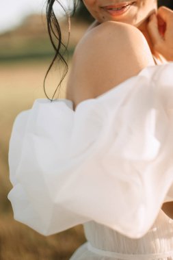 The bride in a white airy wedding dress with a deep neckline holds a mean dress with her hands. Close-up