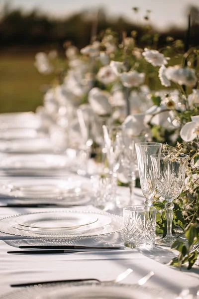 Decor for a wedding ceremony in a picturesque meadow. Wildflowers, crystal glasses, crystal plates, beautiful wedding tableware
