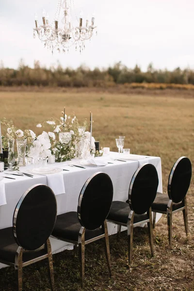 The delicate decor of the wedding banquet table is in pastel colors. Wildflowers, crystal glassware, candles. crystal chandelier on top, illuminating the table.