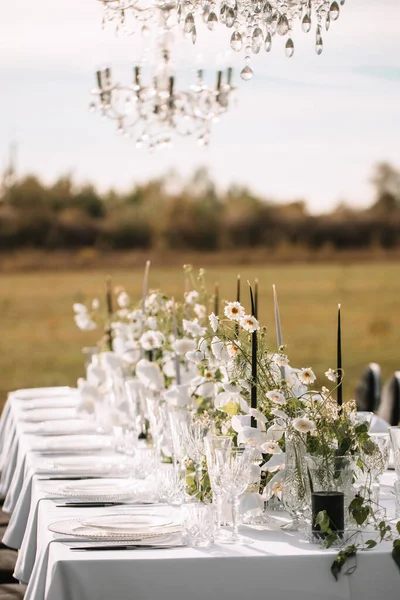 The delicate decor of the wedding banquet table is in pastel colors. Wildflowers, crystal glassware, candles. crystal chandelier on top, illuminating the table.