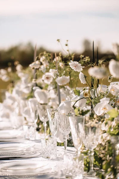 Decor for a wedding ceremony in a picturesque meadow. Wildflowers, crystal glasses, crystal plates, beautiful wedding tableware