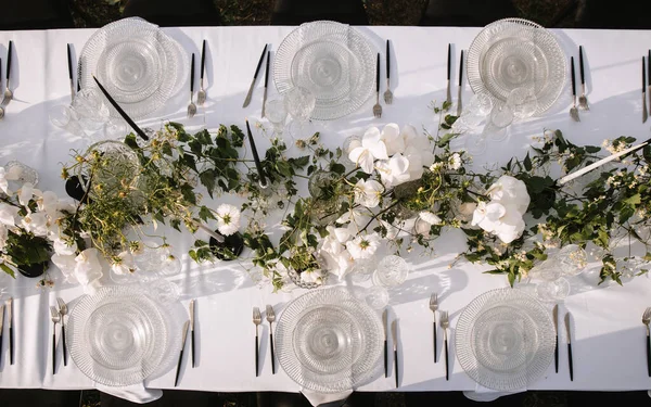 Decor for a wedding ceremony in a picturesque meadow. Wildflowers, crystal glasses, crystal plates, beautiful wedding tableware