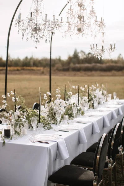 The delicate decor of the wedding banquet table is in pastel colors. Wildflowers, crystal glassware, candles. crystal chandelier on top, illuminating the table.
