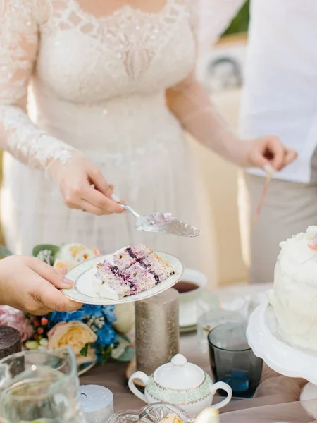 A piece of wedding cake with red cream lies on a plate. In the background is a cake decorated with flowers and a served banquet table.