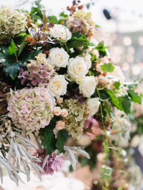 Wedding bouquet in gentle tones of white and pink roses, dry hydrangea, barberry twigs, and green leaves. In the background is a flower decoration.