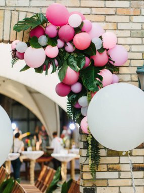 The decor of small white and pink balloons with orchid leaves against a brick wall.